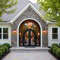 Arched Black Metal Double Doors With Ornate Scrollwork and Stone Facade
