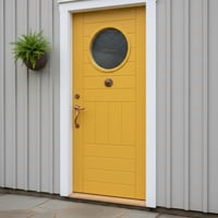 Yellow Plank Door With Round Window, Bronze Medallion, and Gray Stone Paving